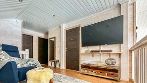 Un salon moderne avec un canapé bleu, un pouf moelleux, une grande télévision et des étagères en bois.