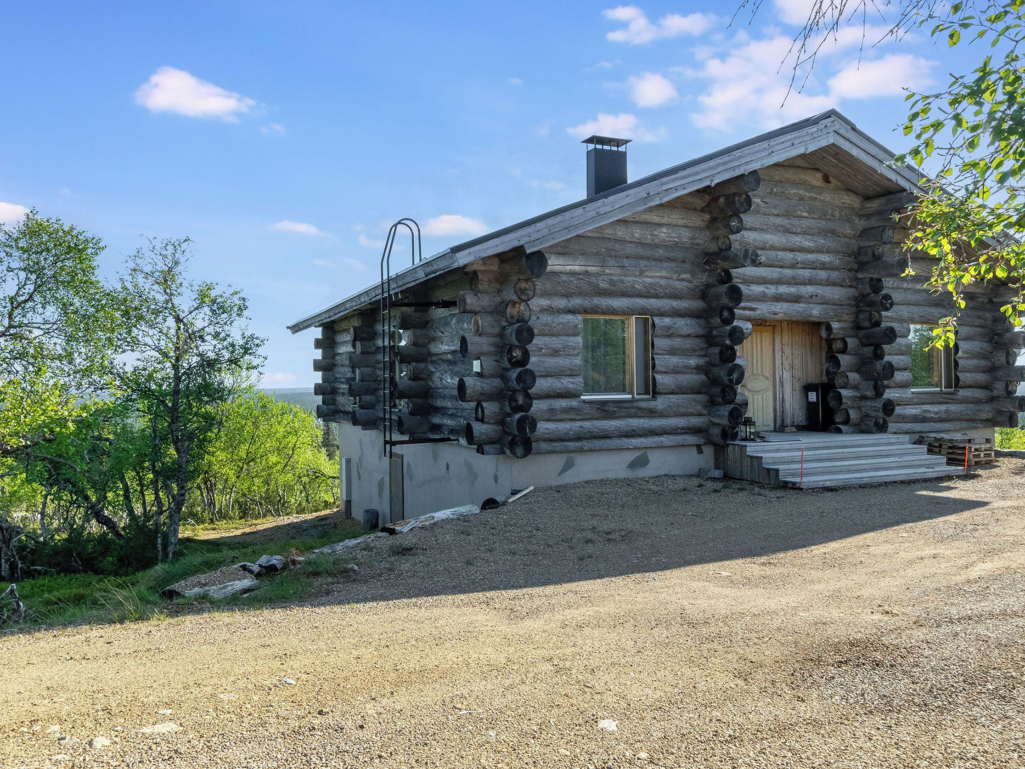 Une cabane en rondins avec une allée en gravier et une vue sur la forêt environnante.