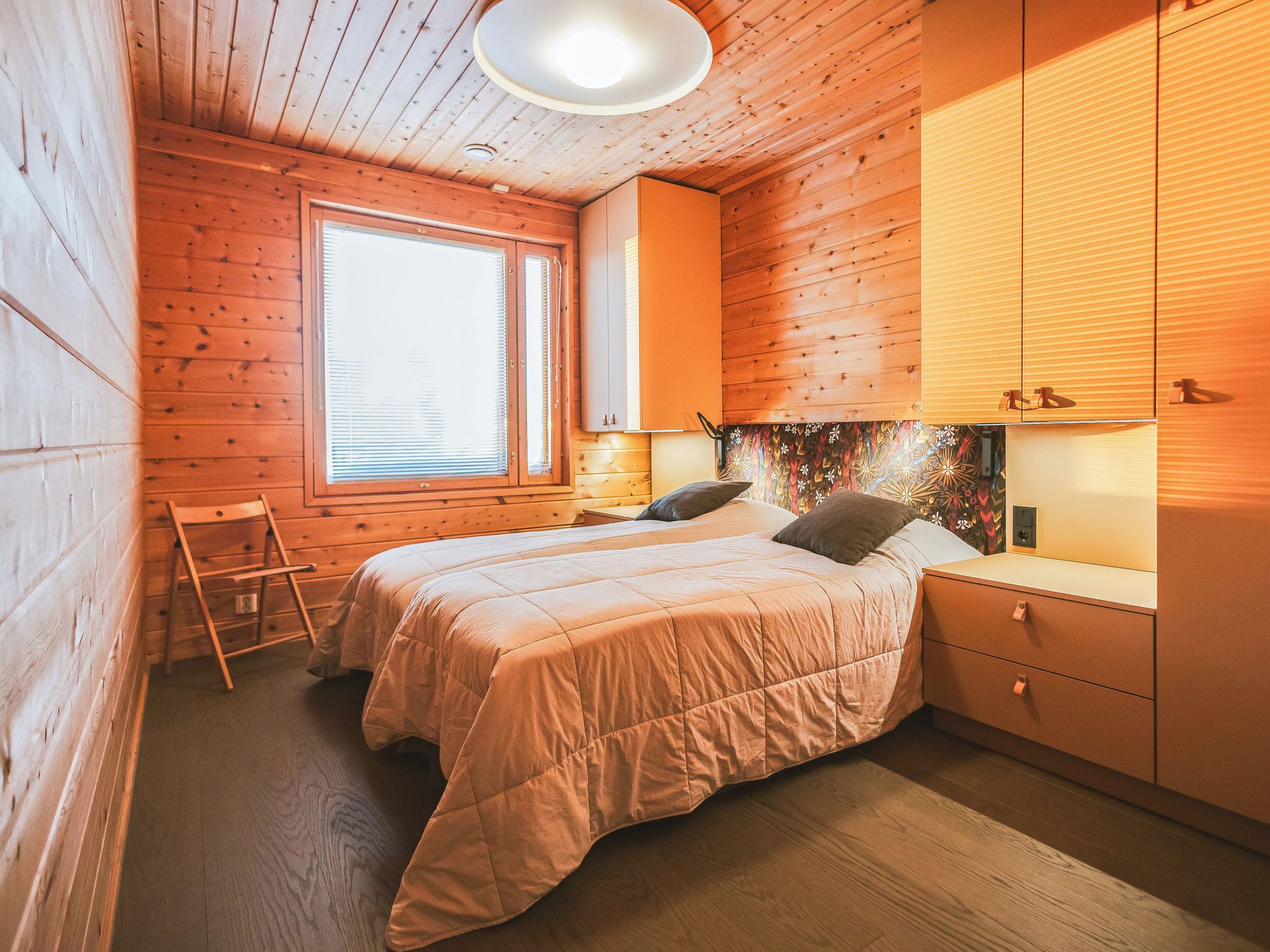 Une pièce chaleureuse en bois, avec un lit, une fenêtre et une table de chevet.