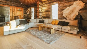 Et interiør af en træhytte med en stor, L-formet sofa, en pejs og en pelslæg.