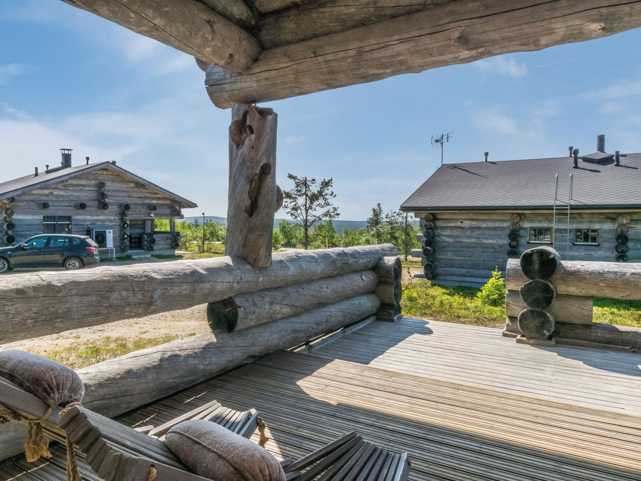 A wooden deck with logs, a bench, and a car parked in the background.