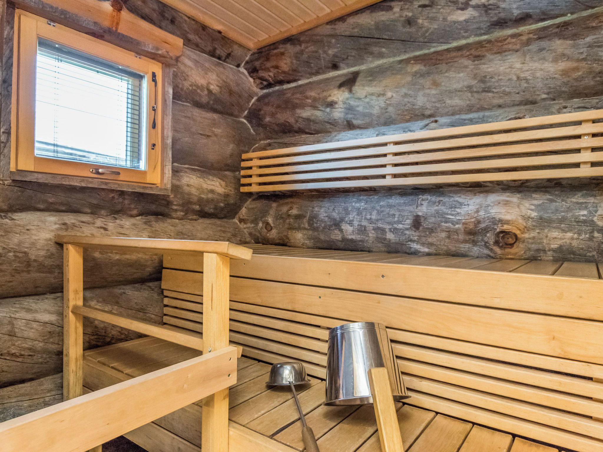 A wooden sauna with benches and a metal bucket.