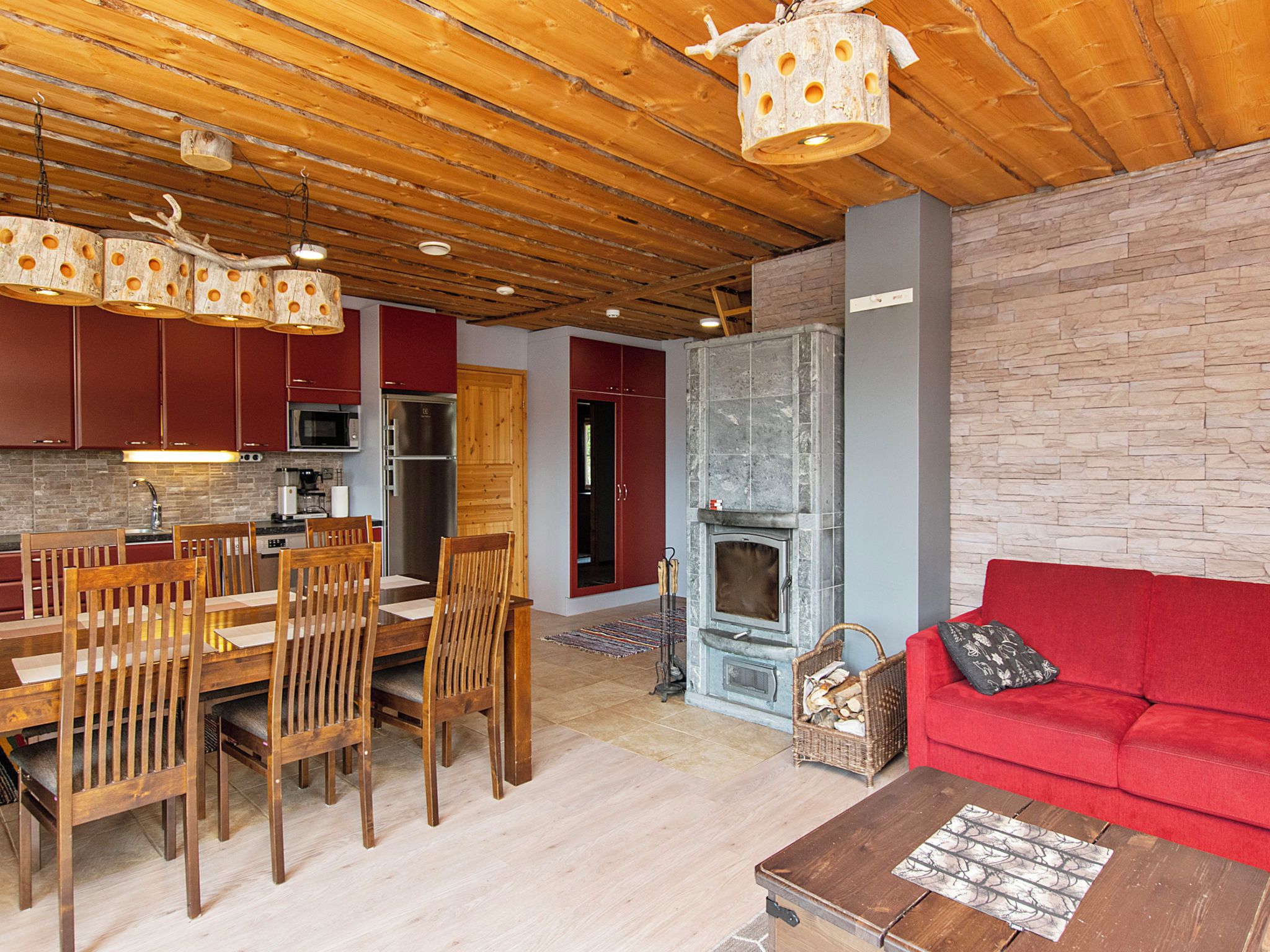 Un interior acogedor con comedor, cocina y sala de estar, que presenta techos de madera, una chimenea y un sofá rojo.