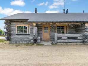 A log cabin with a wooden door, two windows with shutters, and a chimney.