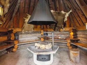 A rustic cabin interior with a central stone fireplace, wooden logs, and a bear skull on the wall.