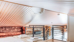Ein modernes Schlafzimmer mit schrägen Wänden, einem Bett mit weißen Leinen, einer flauschigen beige Decke und Blick auf eine Steinsäule durch eine Glastür.