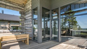 Eine Holzterrasse mit einer Bank, Glastüren zum Gleitschieben und Blick ins Freie.