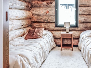 Quarto de cabana de toras com duas camas, uma janela e uma mesinha de cabeceira.