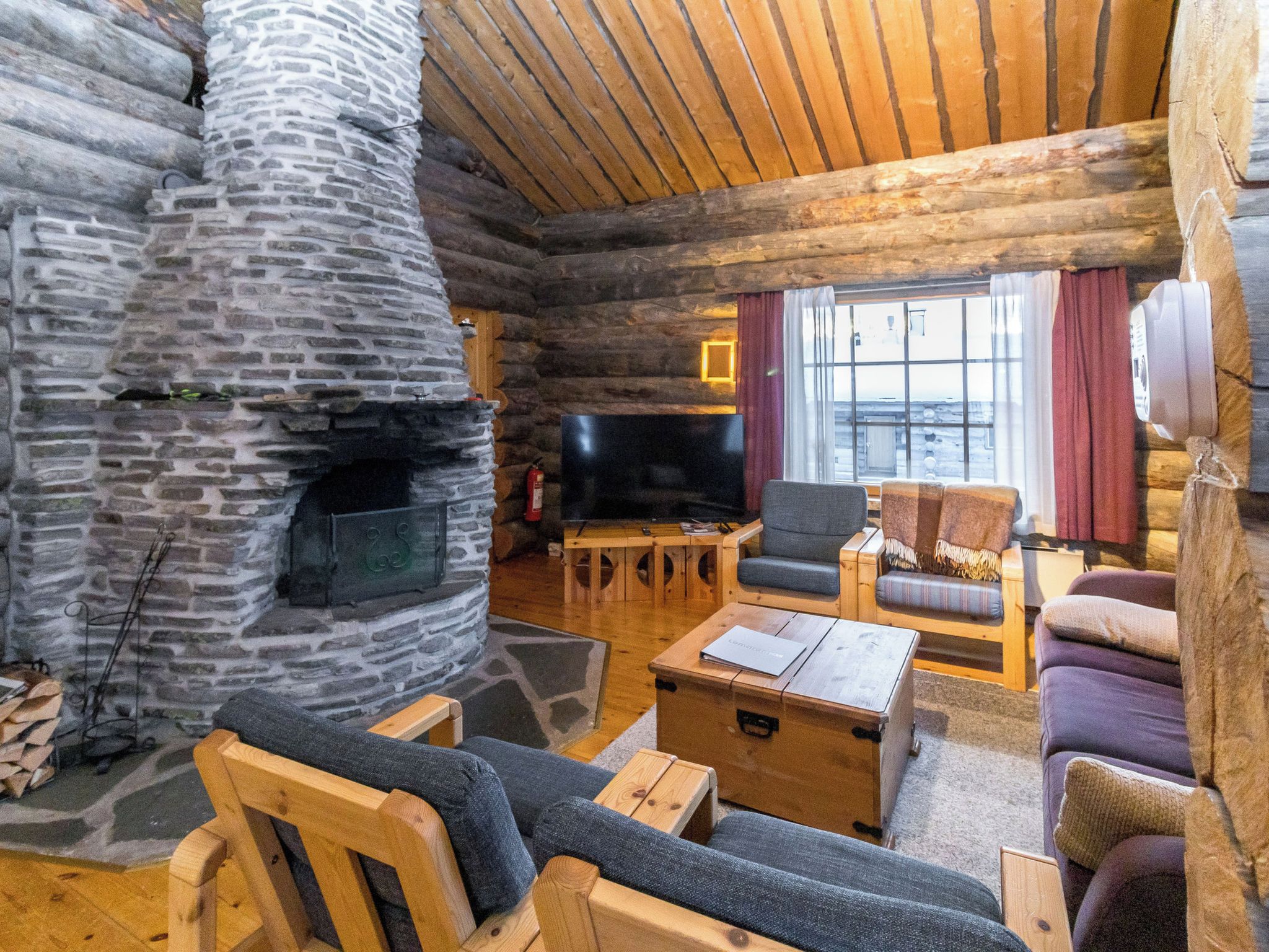 L’intérieur d’une cabane en rondins, avec une cheminée en pierre, des meubles en bois et un téléviseur.