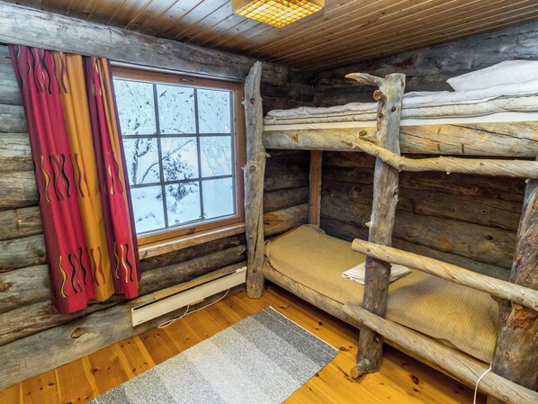 A cabin interior with a bunk bed, a window with a view of snow-covered trees, and a heater on the floor. - Kultarinne by Interhome (Inari)