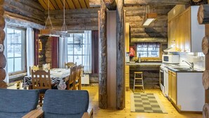 A log cabin interior with a dining area, kitchen, and a large wooden beam structure.