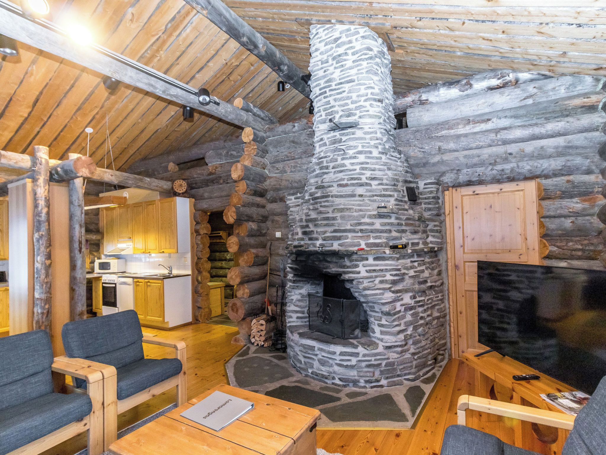 Een knus blokhutinterieur met een stenen open haard, houten meubels en een keukenhoek.