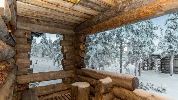 A log cabin with a wooden deck and a view of a snowy forest.