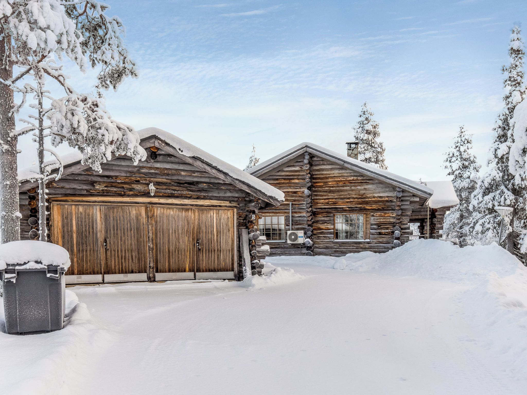 A log cabin with a large garage door, surrounded by snow-covered trees.