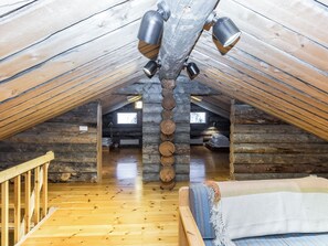A log cabin interior with a wooden floor, a bed with a striped blanket, and a ceiling with hanging lamps. - Kultarinne by Interhome (Inari)