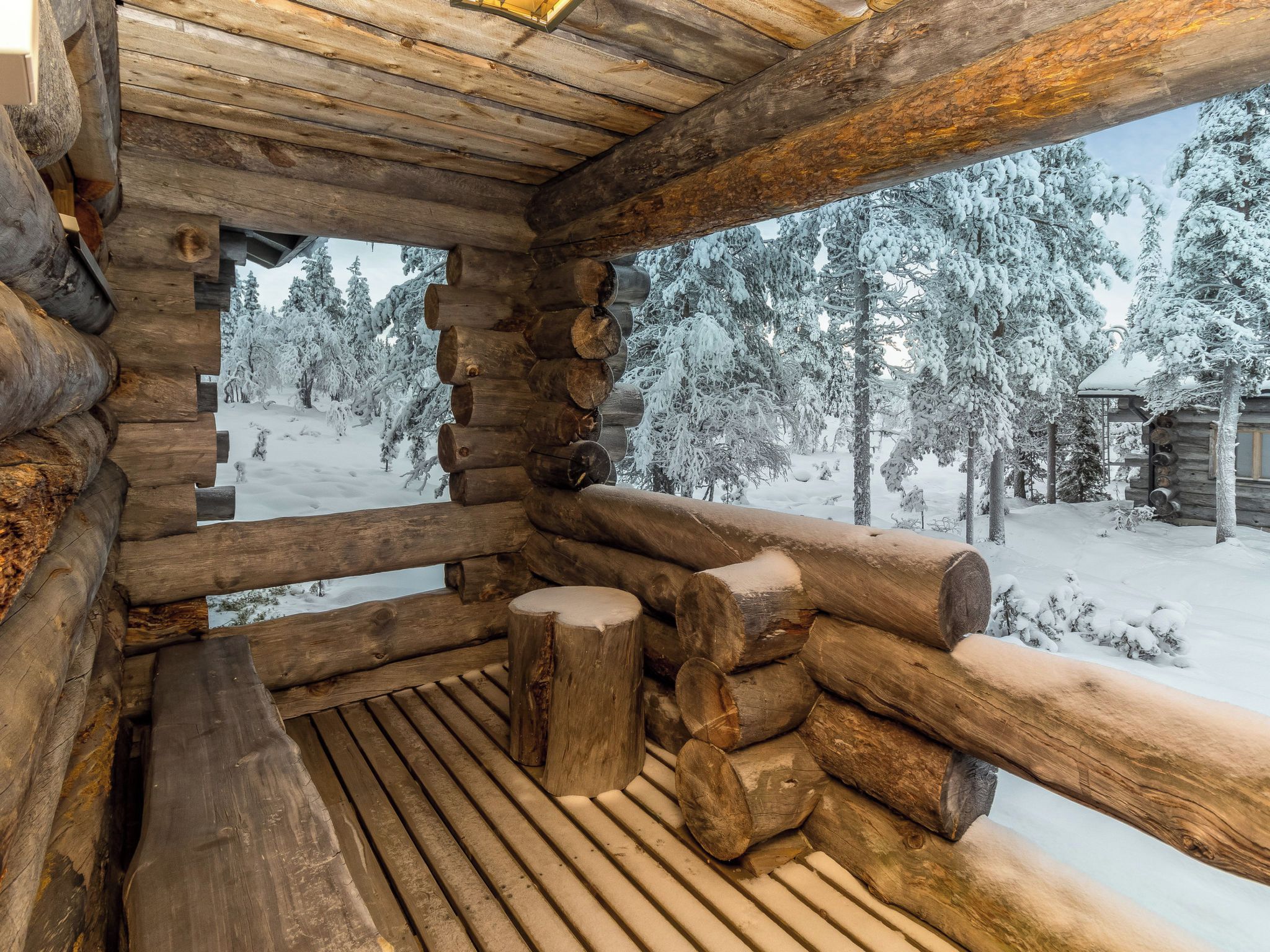 L'intérieur d'une cabane en rondins, avec un banc en bois et une vue sur une forêt enneigée.