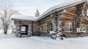 A log cabin with a snow-covered roof and windows, surrounded by snow.