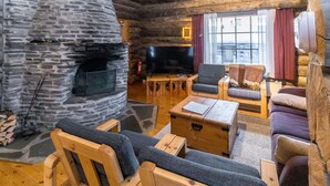 A log cabin interior with a stone fireplace, wooden furniture, and a television.