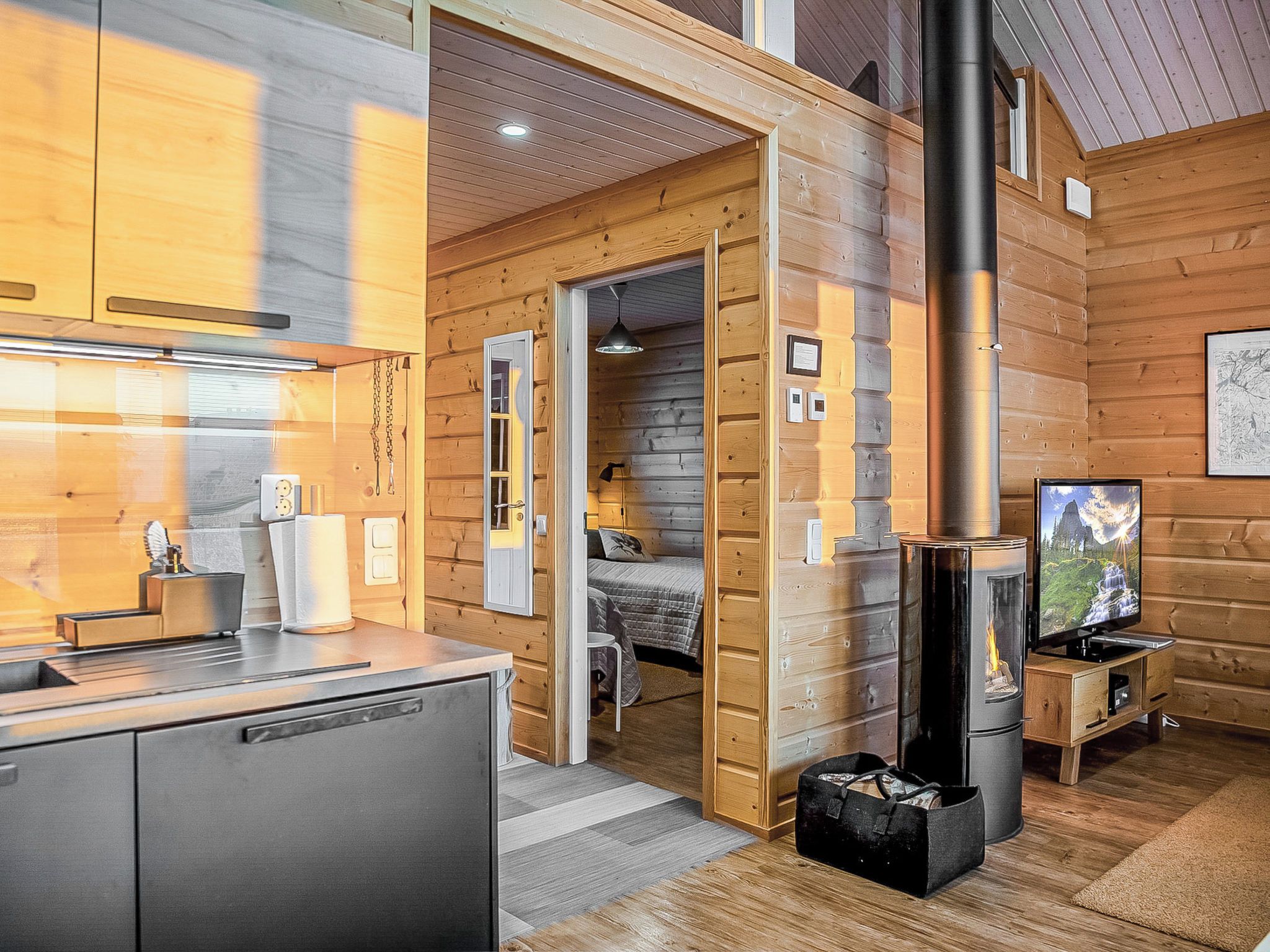 A cozy cabin interior with a kitchen, a sleeping area, and a fireplace.