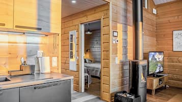 A cozy cabin interior with a kitchen, a sleeping area, and a fireplace.