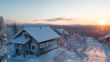 A wooden cabin surrounded by snow-covered trees and a clear sky.