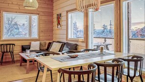 A cozy cabin interior with a wooden interior, a dining area, and large windows with snowy views.
