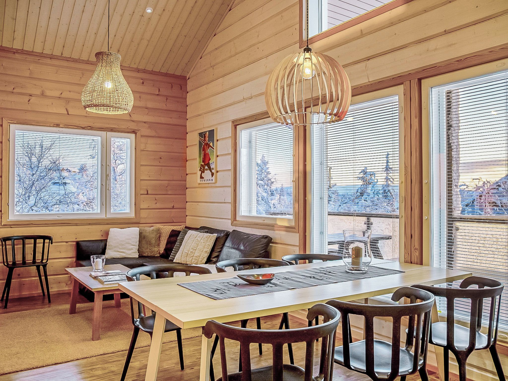 A cozy cabin interior with a wooden interior, a dining table with chairs, and large windows with blinds.