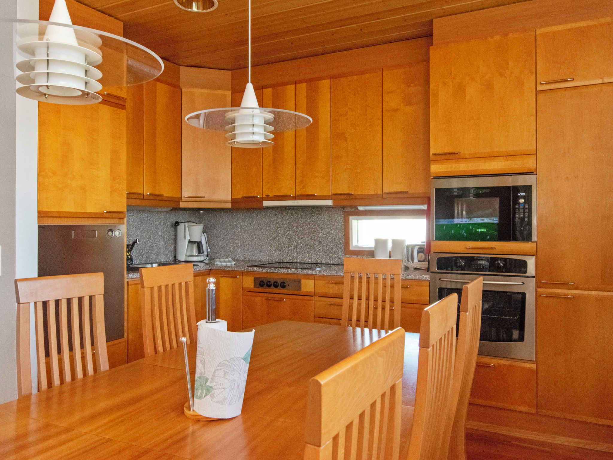 Een moderne keuken met houten kastjes, een eettafel, stoelen, een koffiezetapparaat en een magnetron.