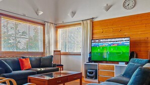 Un salon avec un canapé, une table basse et un téléviseur diffusant un événement sportif.