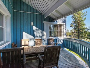 Une terrasse en bois avec une table et des chaises, une fenêtre avec des volets et une rambarde bleue.