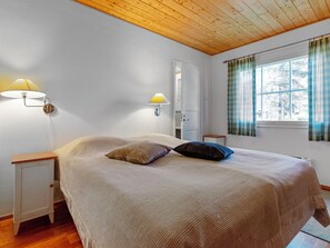 A bedroom with a bed, two bedside tables, a nightstand, a window with curtains, and a door.