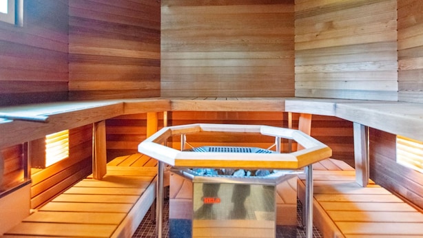 Un sauna avec des murs et des bancs en bois, un système de chauffage central et une porte en verre.