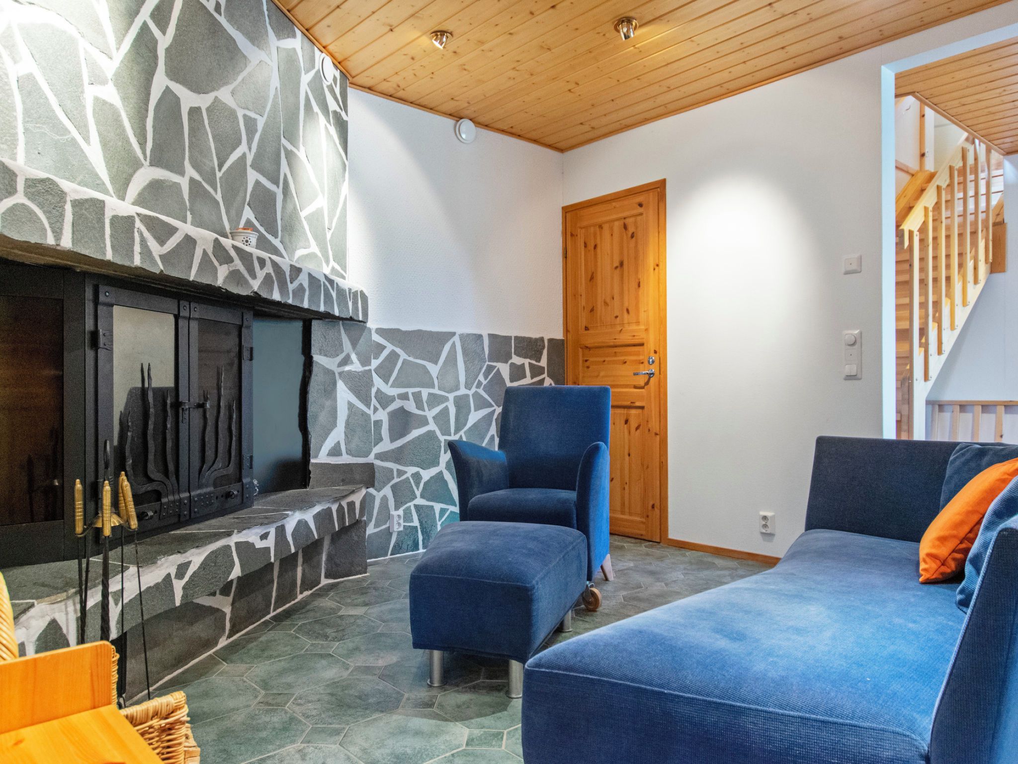 A cozy living room with a stone fireplace, a wooden door, and a staircase.