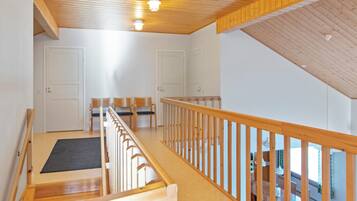 A spacious room with a wooden ceiling, a balcony with a railing, and a view of a dining area.