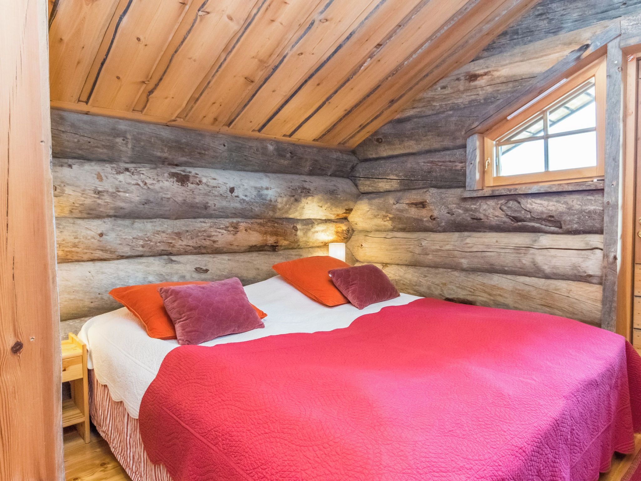 Une chambre dans un chalet en rondins, avec un lit, des oreillers et une fenêtre.