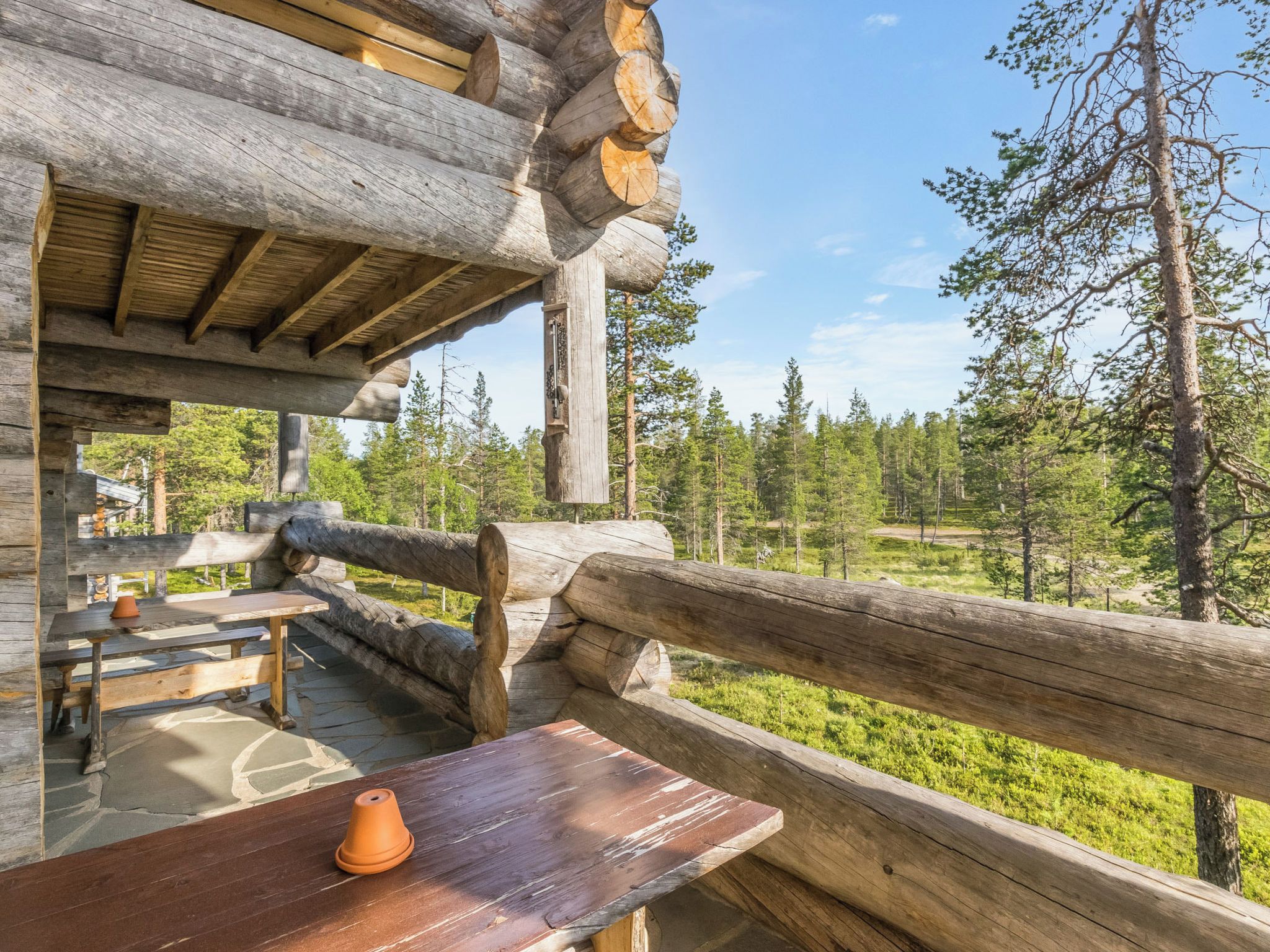 Une cabane en bois rustique, dotée d’une terrasse en bois et d’une table sur laquelle est posé un pot en terre cuite.