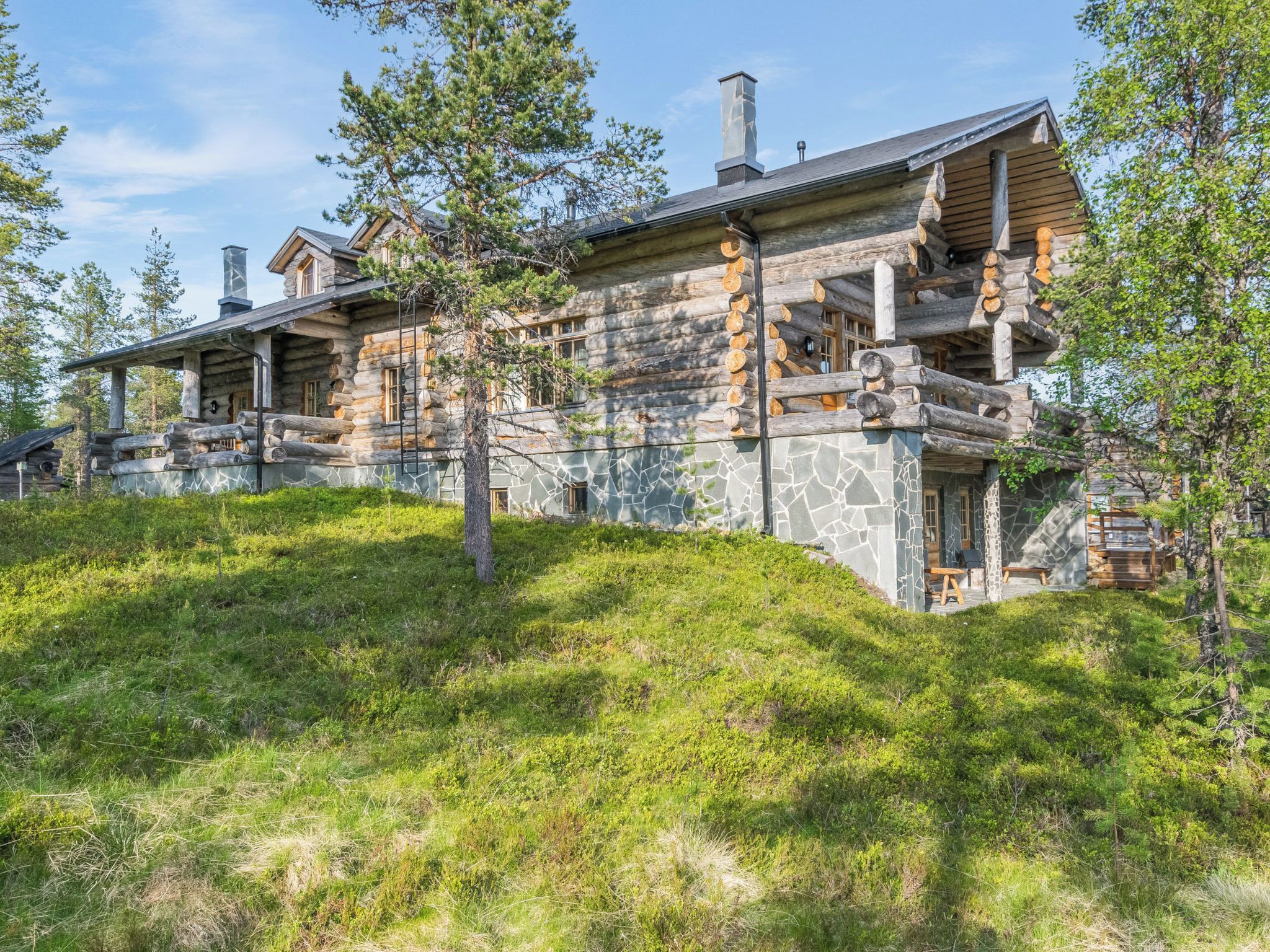 A log cabin with a stone facade, multiple chimneys, and a porch with outdoor seating.
