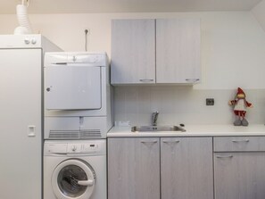 Une cuisine compacte équipée d’un lave-linge, d’un sèche-linge, d’un évier et de placards.