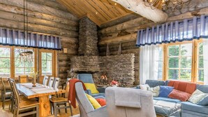 Interior de una cabaña de madera con comedor, chimenea y sala de estar con sofá y sillones.