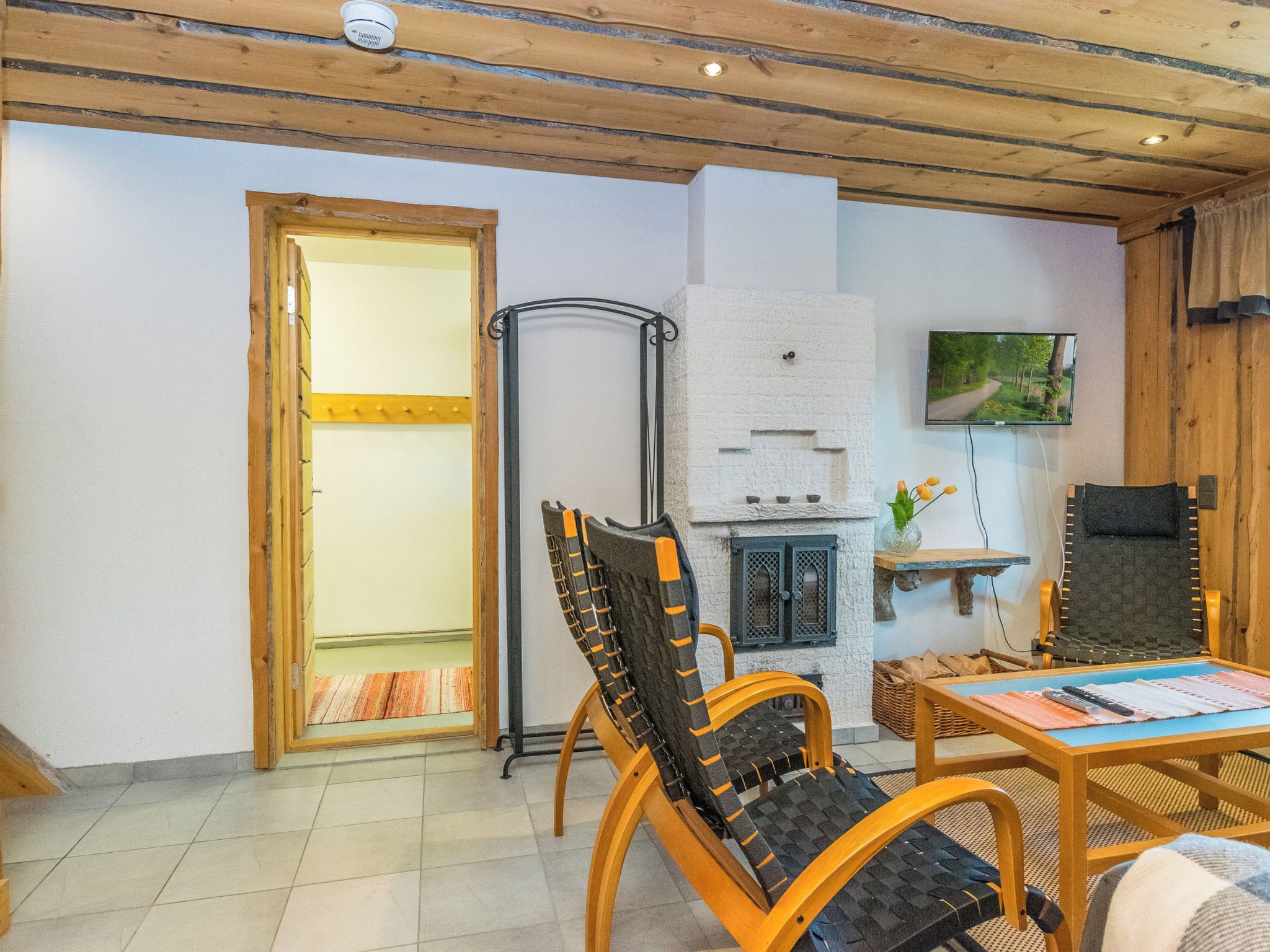 Een gezellige kamer met houten plafond, een open haard, een televisie en een eethoek met stoelen en een tafel.