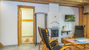 Een gezellige kamer met houten plafond, een open haard, een televisie en een eethoek met stoelen en een tafel.