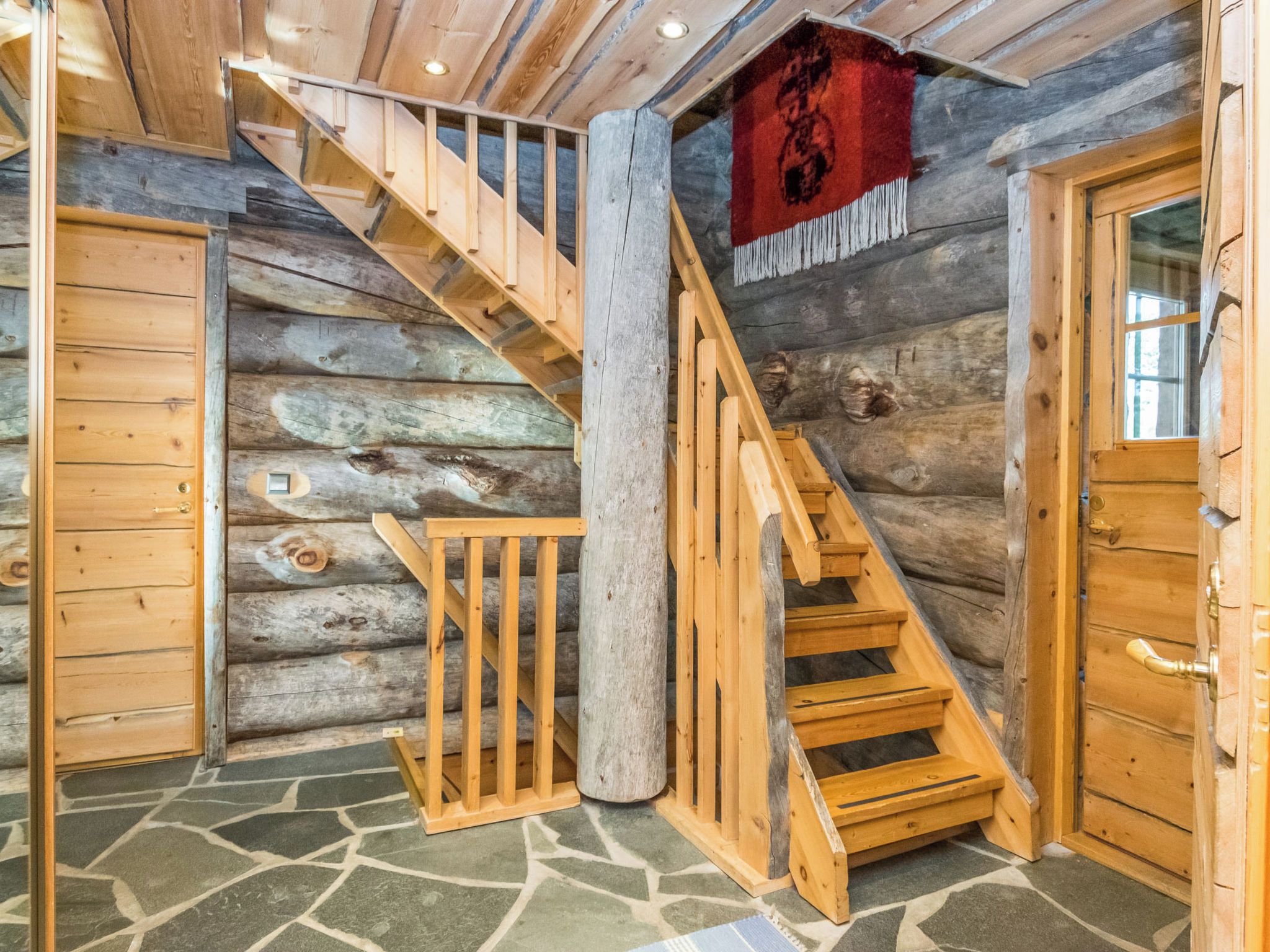 L’intérieur d’une cabane en rondins, avec un escalier en bois, un sol en pierre et un drapeau rouge.