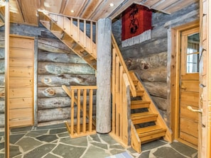 A log cabin interior with a wooden staircase, stone flooring, and a red flag.