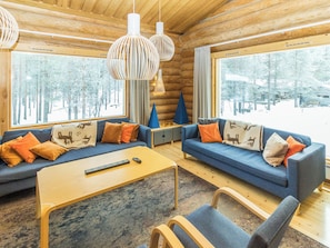 A log cabin interior with two sofas, a coffee table, and a view of a snowy forest.