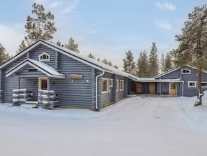 A log cabin hotel with a snow-covered driveway and surrounding trees.