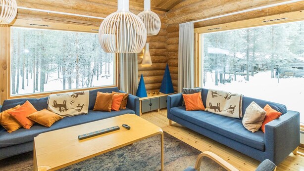A cozy log cabin interior with two sofas, a coffee table, and a TV remote on the table.