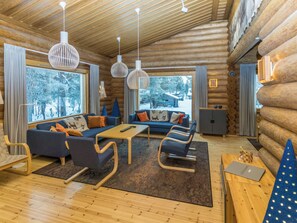 A log cabin interior with a sofa set, wooden flooring, and large windows.