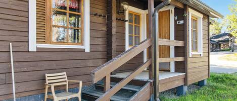 A wooden cabin with a wooden staircase leading to a porch, a bench, and a window with shutters.