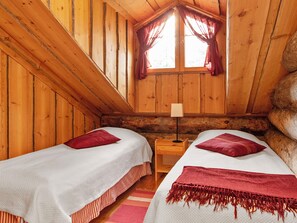 A cabin with two beds, a nightstand, a lamp, and a large rock.