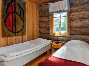 A cabin-style room with two single beds, a wooden wall, a window with a curtain, and a rug with a circular pattern.